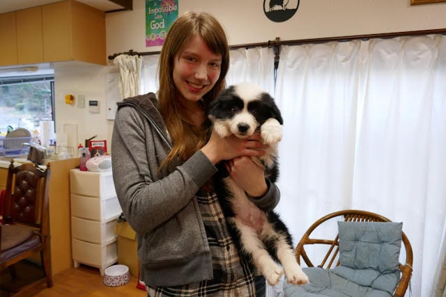 女性と子犬が室内で笑顔でポーズをとる写真.